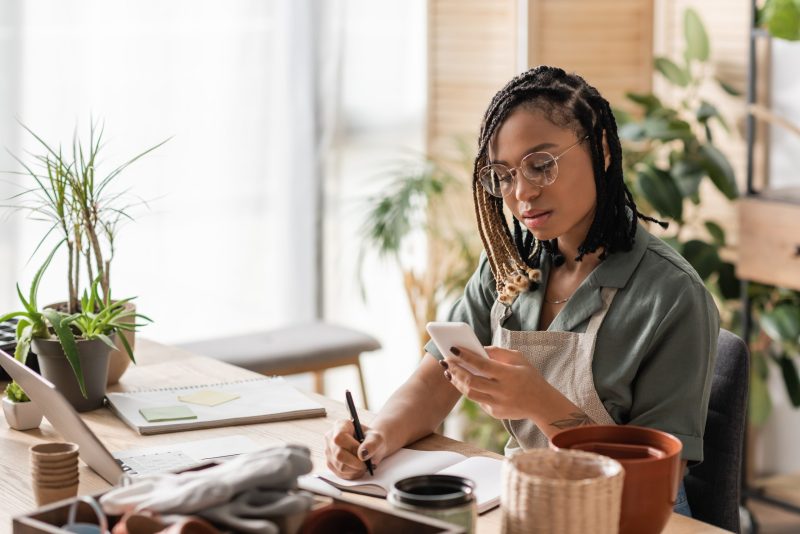 Young,African,American,Florist,In,Eyeglasses,Looking,At,Smartphone,And