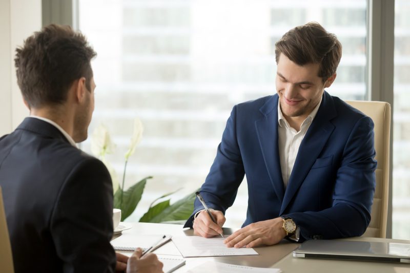 Smiling,Businessman,Signing,Paper,At,Meeting,,Satisfied,Entrepreneur,Concludes,Contract,